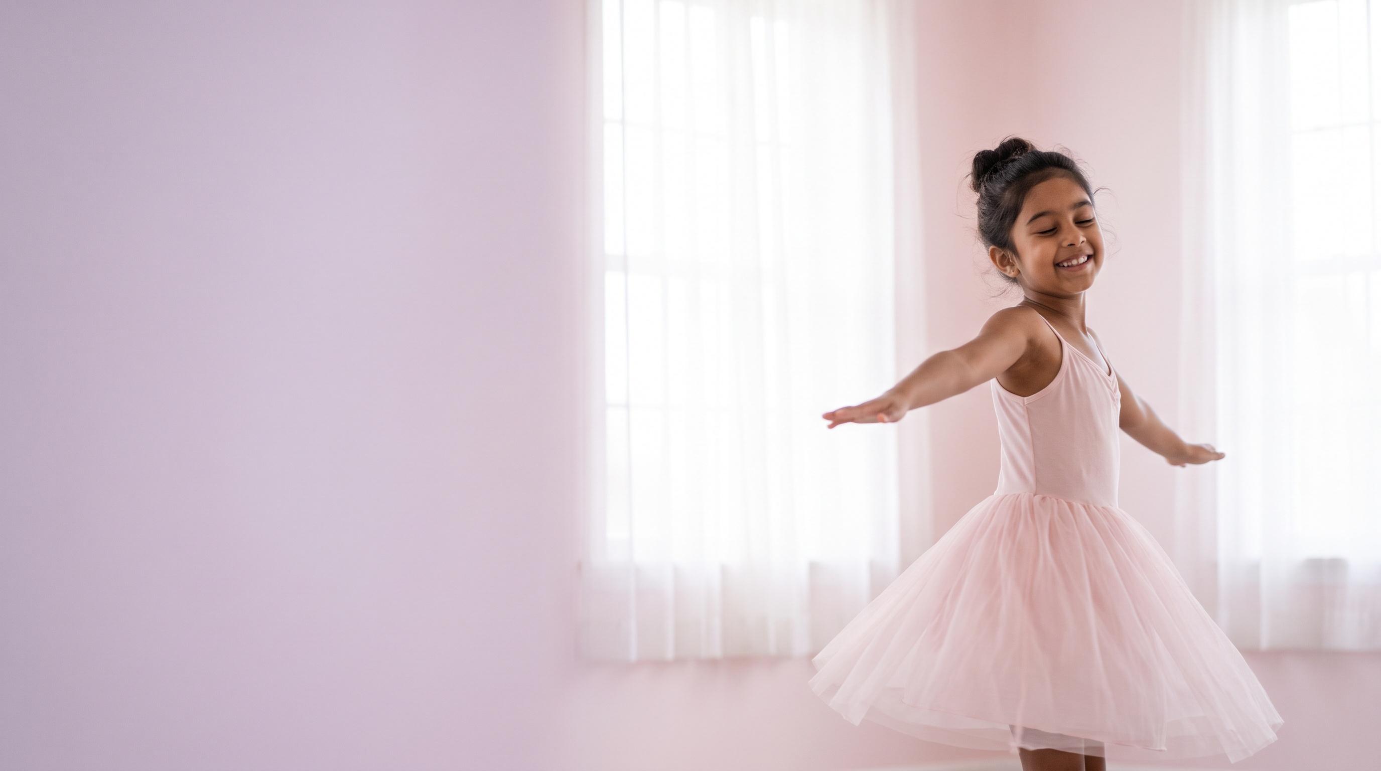 A young dancer spinning with her arms open wide in a sunlit studio